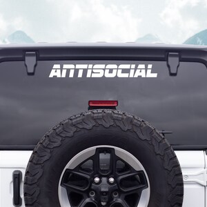 May include: White "ANTISOCIAL" decal on the back window of a white Jeep Wrangler. The spare tire is visible in the lower right corner.