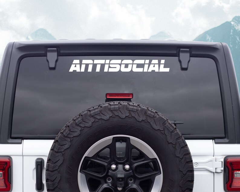May include: White "ANTISOCIAL" decal on the back window of a white Jeep Wrangler. The spare tire is visible in the lower right corner.