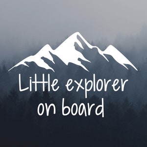 Peut inclure: Une silhouette blanche d'une chaîne de montagnes avec le texte "Little explorer on board" en blanc sur un fond de forêt brumeuse.