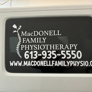 May include: White vinyl decal on a black background with the text "MacDonnell Family Physiotherapy" and the phone number "613-935-5550". The website address "www.macdonnellfamilyphysio.com" is also included.