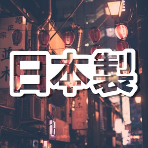 May include: A close-up of a street in Japan with red lanterns hanging from wires. The text "日本製" is superimposed on the image, which translates to "Made in Japan".