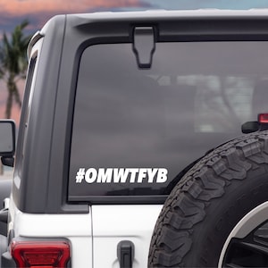 May include: White Jeep with a #OMWTFYB sticker on the back window. The Jeep is parked on a beach with a palm tree in the background.