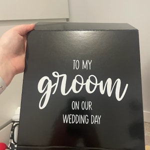 May include: Black gift box with white text that reads "To my groom on our wedding day".