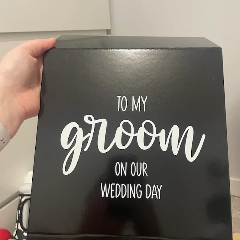 May include: Black gift box with white text that reads "To my groom on our wedding day".