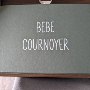 K&ouml;nnte beinhalten: Eine gr&uuml;ne Box mit dem Text "B&Eacute;B&Eacute; COURNOYER" in wei&szlig;en Buchstaben.