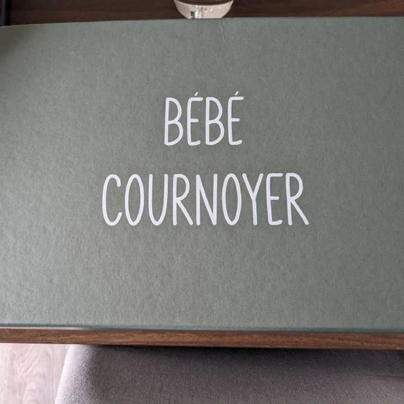 K&ouml;nnte beinhalten: Eine gr&uuml;ne Box mit dem Text "B&Eacute;B&Eacute; COURNOYER" in wei&szlig;en Buchstaben.