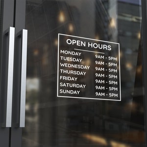 Peut inclure: Une porte en verre avec une affiche blanche et du texte noir indiquant les heures d'ouverture du magasin. L'affiche indique "OPEN HOURS" et liste les jours de la semaine avec les heures correspondantes de 9h à 17h.
