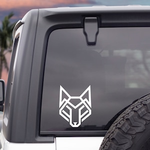 May include: A white geometric wolf head decal on the rear window of a silver SUV. The decal is a modern, minimalist design.