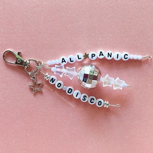 May include: A handmade keychain with the words "ALL PANIC NO DISCO" spelled out in white letter beads. The keychain features a small disco ball, star charms, and clear crystal-like beads, all attached to a silver-colored clasp.