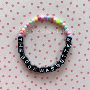 May include: A colorful beaded bracelet with black letter beads spelling out the phrase "The book was better".