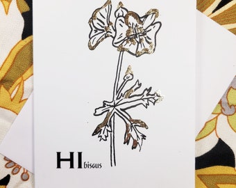 Op de afbeelding: Een witte kaart met een zwarte lijntekening van een bloem met gouden accenten. De tekst "HI bisous" is onder de bloem gedrukt.