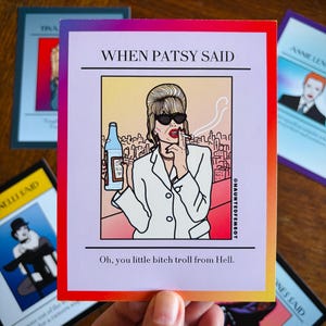 Könnte beinhalten: Eine farbenfrohe Karte mit einer Illustration einer Frau mit Sonnenbrille, die eine Zigarette raucht und eine Flasche hält. Der Text "WHEN PATSY SAID" steht oben, mit dem Zitat "Oh, you little bitch troll from Hell" unten.