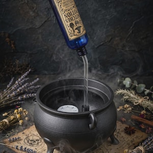 May include: A black cauldron with three legs and a handle, featuring a blue bottle labeled Witches Potion, Dark Forest Apothecary, Salem 1692. A clear tube extends from the bottle into the cauldron, releasing white smoke into the air.