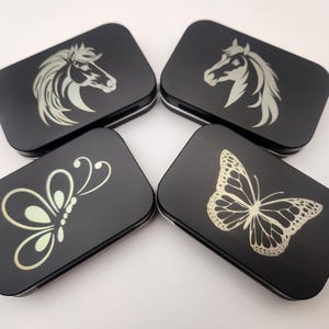 May include: Four black metal tins with different designs. The designs include a horse head, a butterfly, and two different butterflies.