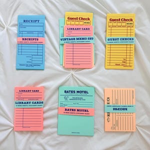 May include: A collection of six rectangular memo pads in various colors including blue, yellow, pink, and green. Each pad features printed text such as Receipt, Guest Check, Library Card, Bates Motel, and Recipes, with lines for writing notes.