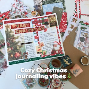 May include: A festive Christmas journaling spread with decorative elements. The open journal features a Christmas tree illustration, the words "Merry Christmas," and handwritten notes. Surrounding the journal are washi tape, stickers, and other holiday-themed stationery.