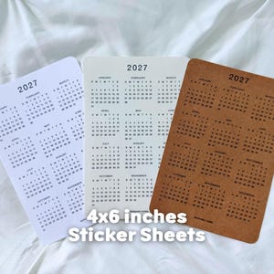 May include: Three rectangular 4x6 inches sticker sheets featuring the 2027 calendar year. One sheet is white with black text, one is off-white with black text, and one is brown kraft paper with black text. Each sheet displays all twelve months.