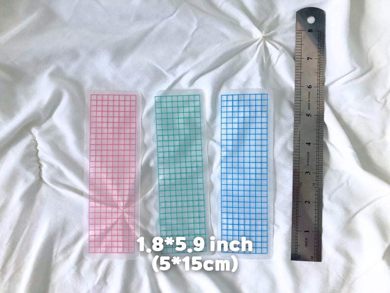 May include: Three grid-patterned bookmarks in pink, green, and blue, each measuring 1.8 x 5.9 inches. A metal ruler is placed next to the bookmarks. The text on the image reads "1.8*5.9 inch (5*15cm)".