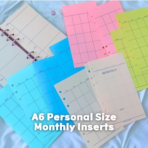 May include: A collection of A6 personal size monthly planner inserts in various colors including neon pink, neon yellow, bright blue, and cream. Each sheet features a printed monthly calendar grid with days of the week and punch holes for binding.