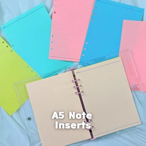 May include: A collection of A5 note inserts featuring a clear binder with cream-colored grid paper, alongside loose sheets in neon yellow, bright turquoise, lined pink, blue, and solid pink, all with pre-punched holes for a six-ring binder system.