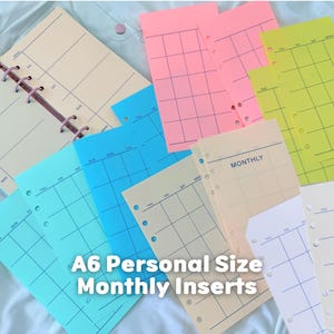 May include: A collection of A6 personal size monthly planner inserts in various colors including pink, yellow, blue, and cream. Each sheet features a grid layout with days of the week printed at the top and punched holes along the side for binding.