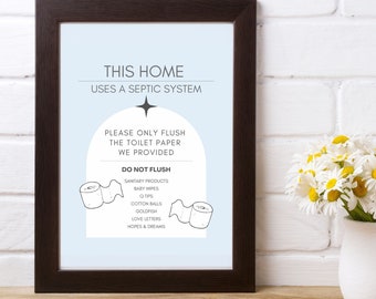May include: A framed print with the text "THIS HOME USES A SEPTIC SYSTEM." The print is 20.3 cm x 25.4 cm and includes a list of items not to flush. The frame is dark brown, and the background is light blue. A vase of white flowers is on the right.
