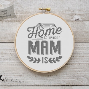 Könnte beinhalten: Ein schwarz-weißes Kreuzstichmuster in einem hölzernen Stickrahmen. Das Muster sagt "Home is where Mam is" mit einem kleinen Haussymbol über dem Text.