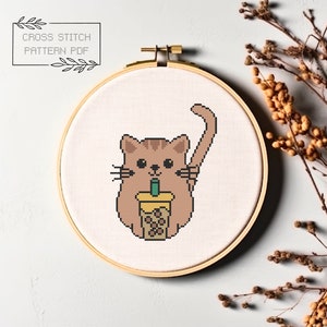 May include: Cross stitch pattern of a brown cat holding a cup of boba tea with a green straw. The cat is sitting on a white background.
