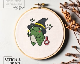 May include: Cross stitch pattern PDF of a green frog wearing a witch's hat and holding a wand and a potion bottle. The text "Stitch a Quote" is below the image.