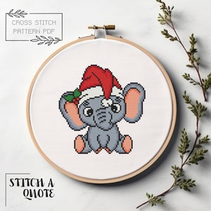 May include: Cross stitch pattern PDF of a gray elephant wearing a red Santa hat with green holly and berries. The pattern is in a white embroidery hoop.