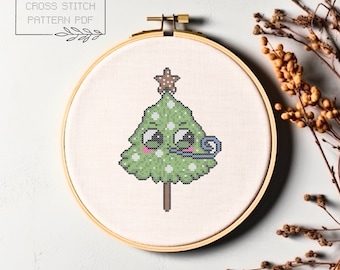 May include: A cross stitch pattern of a green Christmas tree with a star on top. The tree has a cute cartoon face with big eyes and a party blower in its mouth.