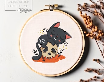 May include: Cross stitch pattern PDF of a black cat sleeping on a skull with orange and yellow accents.