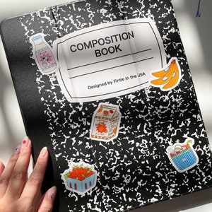 May include: A black and white composition book with a white label that says "COMPOSITION BOOK" and "Designed by Fintie in the USA". There are several colorful stickers on the cover, including a milk carton, a carton of orange juice, a basket of strawberries, a basket of groceries, and a bunch of bananas.