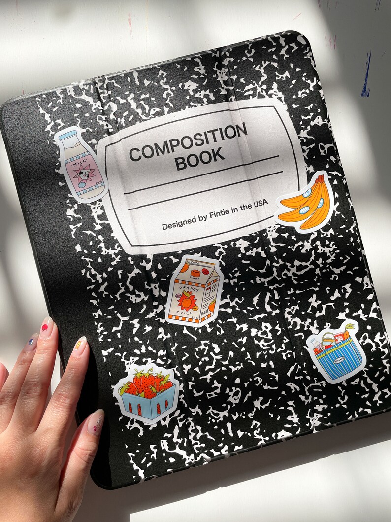 May include: A black and white composition book with a white label that says "COMPOSITION BOOK" and "Designed by Fintie in the USA". There are several colorful stickers on the cover, including a milk carton, a carton of orange juice, a basket of strawberries, a basket of groceries, and a bunch of bananas.