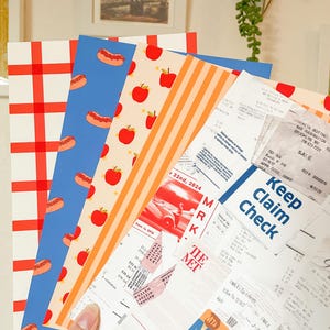 May include: A collection of colorful paper designs featuring patterns of red and white checkered, hot dogs, red apples, and orange stripes. Also included are receipts and a MetroCard, with the text "Keep Claim Check".