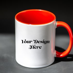 K&ouml;nnte beinhalten: Wei&szlig;er Keramikbecher mit leuchtend rotem Innenraum und Henkel. Der Becher tr&auml;gt den Text "Your Design Here" in schwarzer Schrift. Der Becher steht vor einem dunklen Hintergrund, der seine leuchtenden Farben und sein Design hervorhebt.