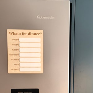 May include: A stainless steel refrigerator with a water dispenser and a magnetic meal planner that says "What's for dinner?" with spaces for each day of the week.