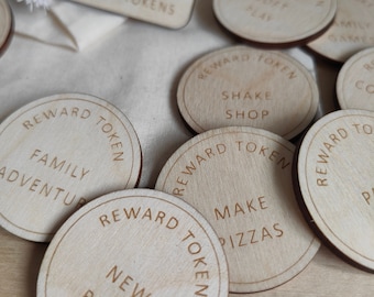 May include: A set of wooden reward tokens with various activities written on them, such as "Make Pizzas", "Shake Shop", "Family Adventure", and "New Book". The tokens are circular and have a light wood color.
