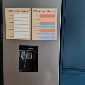 May include: A stainless steel refrigerator with a water dispenser and two magnetic weekly meal planners. The planners have the text "What's for dinner?" and list the days of the week, Sunday through Saturday. One planner has blank spaces for writing in meals, and the other has colored stripes for each day.