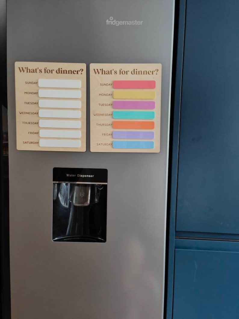 May include: A stainless steel refrigerator with a water dispenser and two magnetic weekly meal planners. The planners have the text "What's for dinner?" and list the days of the week, Sunday through Saturday. One planner has blank spaces for writing in meals, and the other has colored stripes for each day.