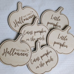 May include: Six wooden pumpkin-shaped ornaments with different Halloween-themed sayings. The sayings include "My First Halloween", "Cutest Pumpkin in the Patch", and "Little Pumpkin".
