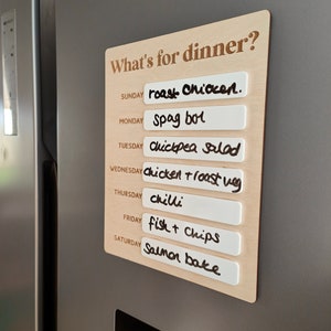 May include: A wooden sign with the text "What's for dinner?" and a list of meals for each day of the week. The meals are written on white labels and include roast chicken, spag bol, chickpea salad, chicken roast veg, chilli, fish and chips, and salmon bake.