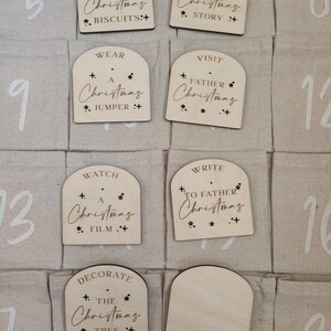 K&ouml;nnte beinhalten: Ein Adventskalender aus Holz mit 12 nummerierten F&auml;chern. Jedes Fach hat eine kleine Holzt&uuml;r mit einer weihnachtlichen Aktivit&auml;t darauf geschrieben. Die Aktivit&auml;ten umfassen "Backen Sie Weihnachtskekse", "Lesen Sie eine Weihnachtsgeschichte", "Tragen Sie einen Weihnachtspullover", "Besuchen Sie den Weihnachtsmann", "Sehen Sie sich einen Weihnachtsfilm an", "Schreiben Sie an den Weihnachtsmann" und "Schm&uuml;cken Sie den Weihnachtsbaum".