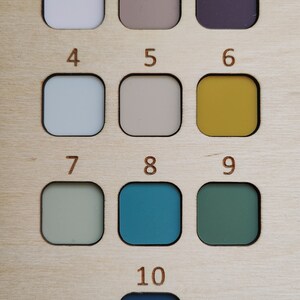 May include: A wooden color chart with ten numbered squares, each containing a different color paint sample. The colors include white, beige, purple, light blue, gray, yellow, green, teal, dark green, and dark blue.