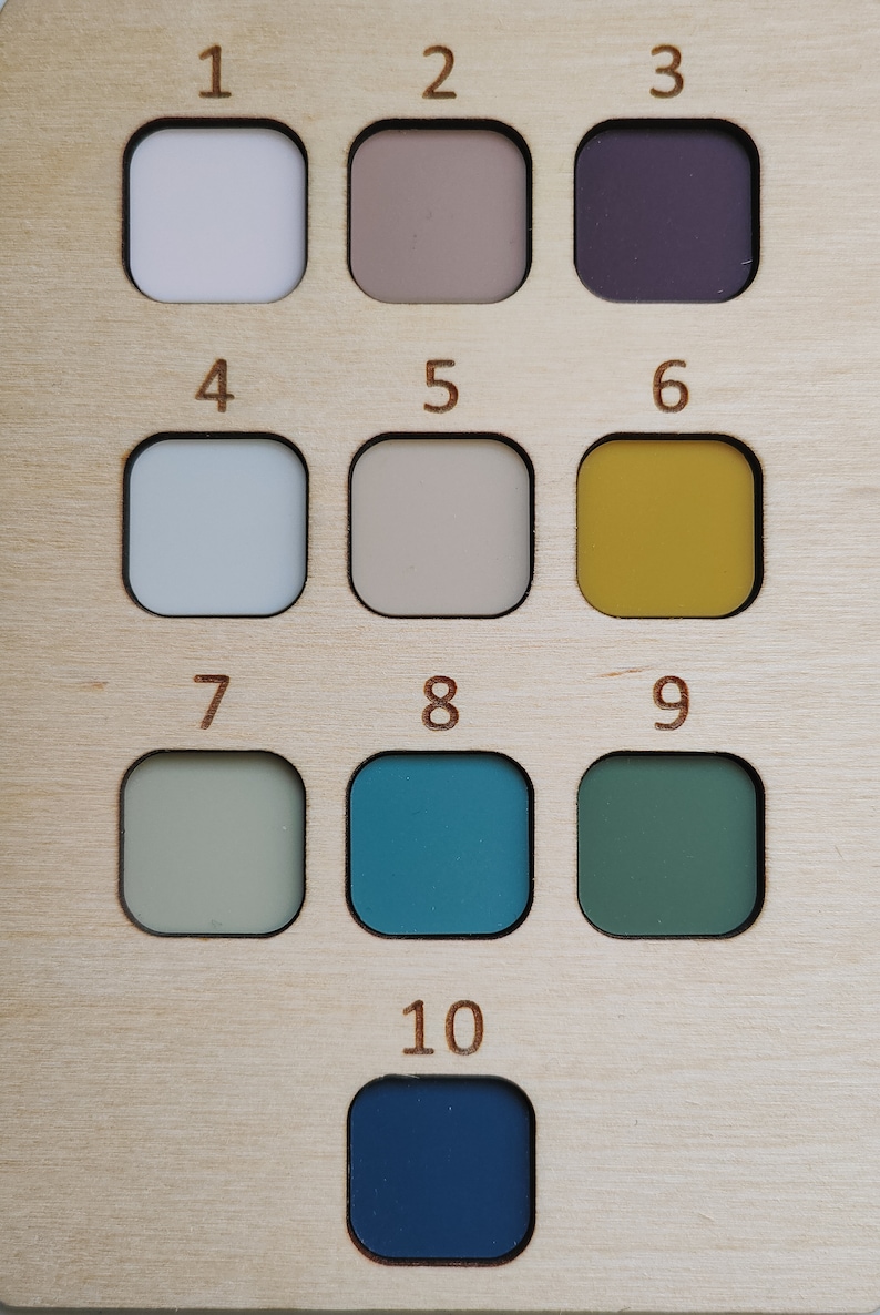 May include: A wooden color chart with ten numbered squares, each containing a different color paint sample. The colors include white, beige, purple, light blue, gray, yellow, green, teal, dark green, and dark blue.