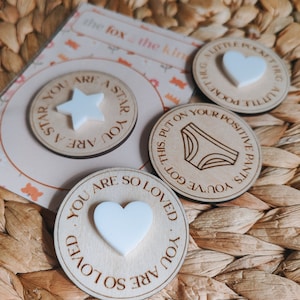 May include: Three wooden circles with inspirational messages and white shapes. The first circle says "You are a star. You are a star." and has a white star shape. The second circle says "You've got this. Put on your positive pants." and has a white underwear shape. The third circle says "You are so loved. You are so loved." and has a white heart shape.