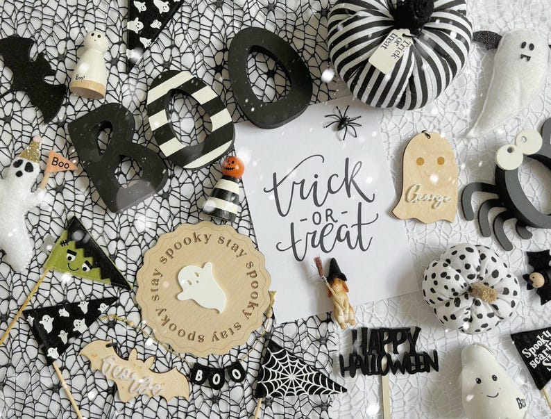 May include: A collection of Halloween decorations including a black and white striped pumpkin, a wooden ghost, a wooden spider, a wooden sign that says "trick or treat", and a wooden sign that says "spooky stay spooky".