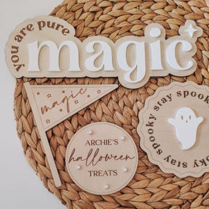 May include: Wooden Halloween decorations with the words "You are pure magic", "magic", "Archie's Halloween Treats", and "Spooky stay spooky stay spooky". The decorations are on a woven wicker background.