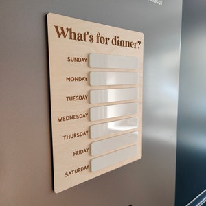 May include: A wooden weekly meal planner with the text "What's for dinner?" and blank white spaces for each day of the week: Sunday, Monday, Tuesday, Wednesday, Thursday, Friday, and Saturday.