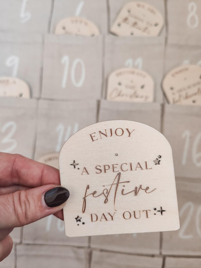 K&ouml;nnte beinhalten: Ein Adventskalender aus Holz mit hellbraunem Hintergrund. Der Kalender hat 24 nummerierte F&auml;cher, jedes mit einem kleinen Holzschild. Das Schild auf dem Bild sagt "Genie&szlig;en Sie einen besonderen festlichen Tag".